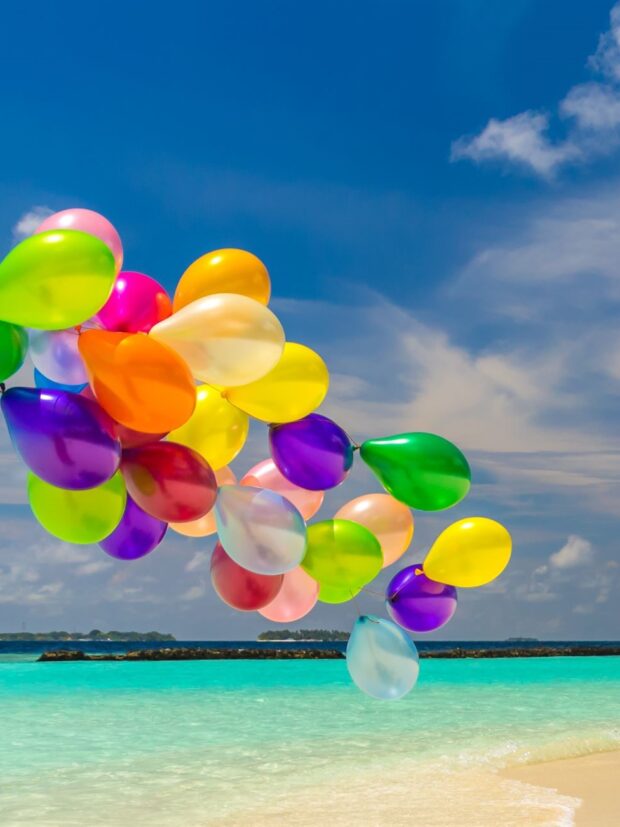 Bunch of colorful balloons flying over tropical ocean