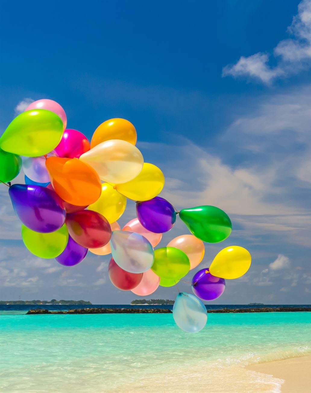 Bunch of colorful balloons flying over tropical ocean